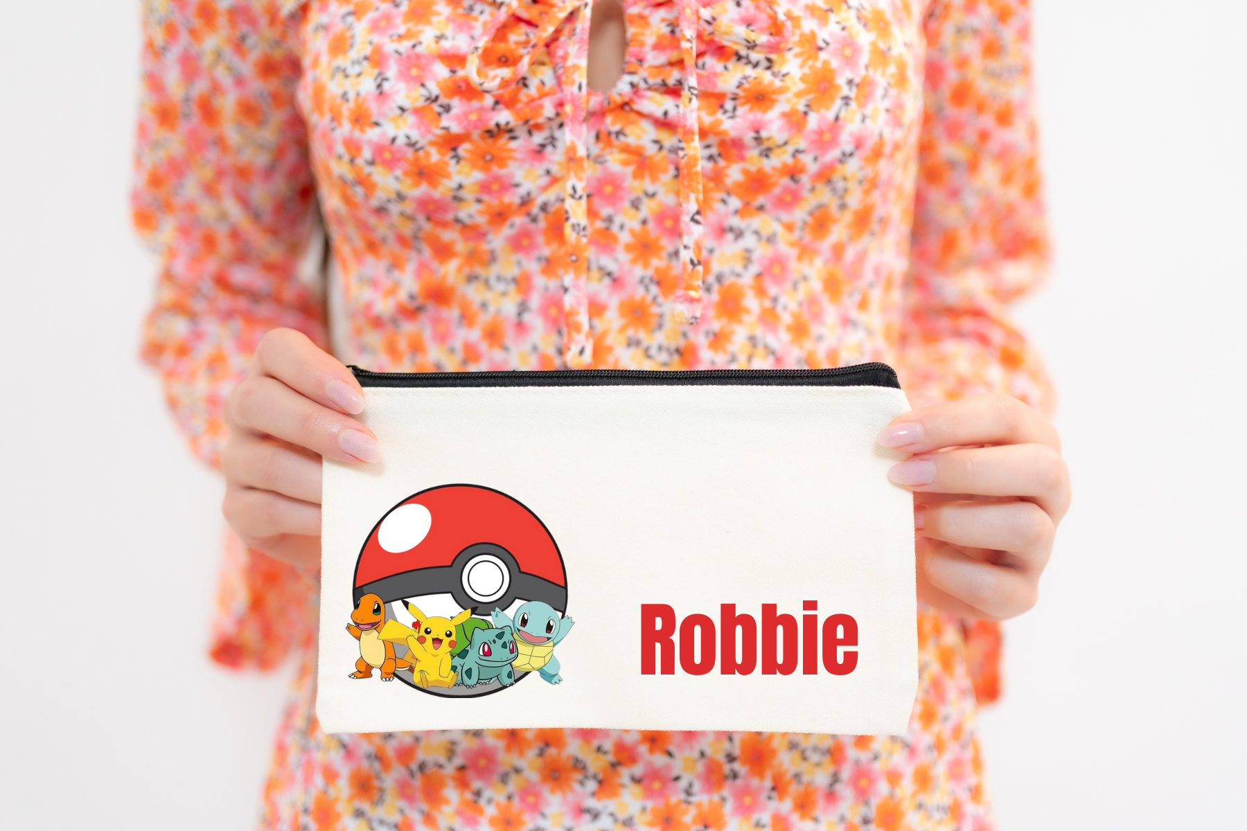 A person holding a multicolored Pokemon pencil case with a character illustration and the name 'Robbie' printed on it.