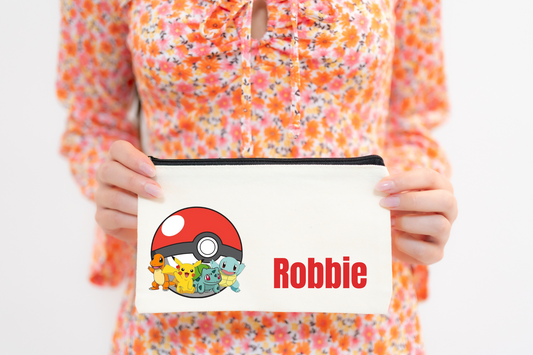 A person holding a multicolored Pokemon pencil case with a character illustration and the name 'Robbie' printed on it.