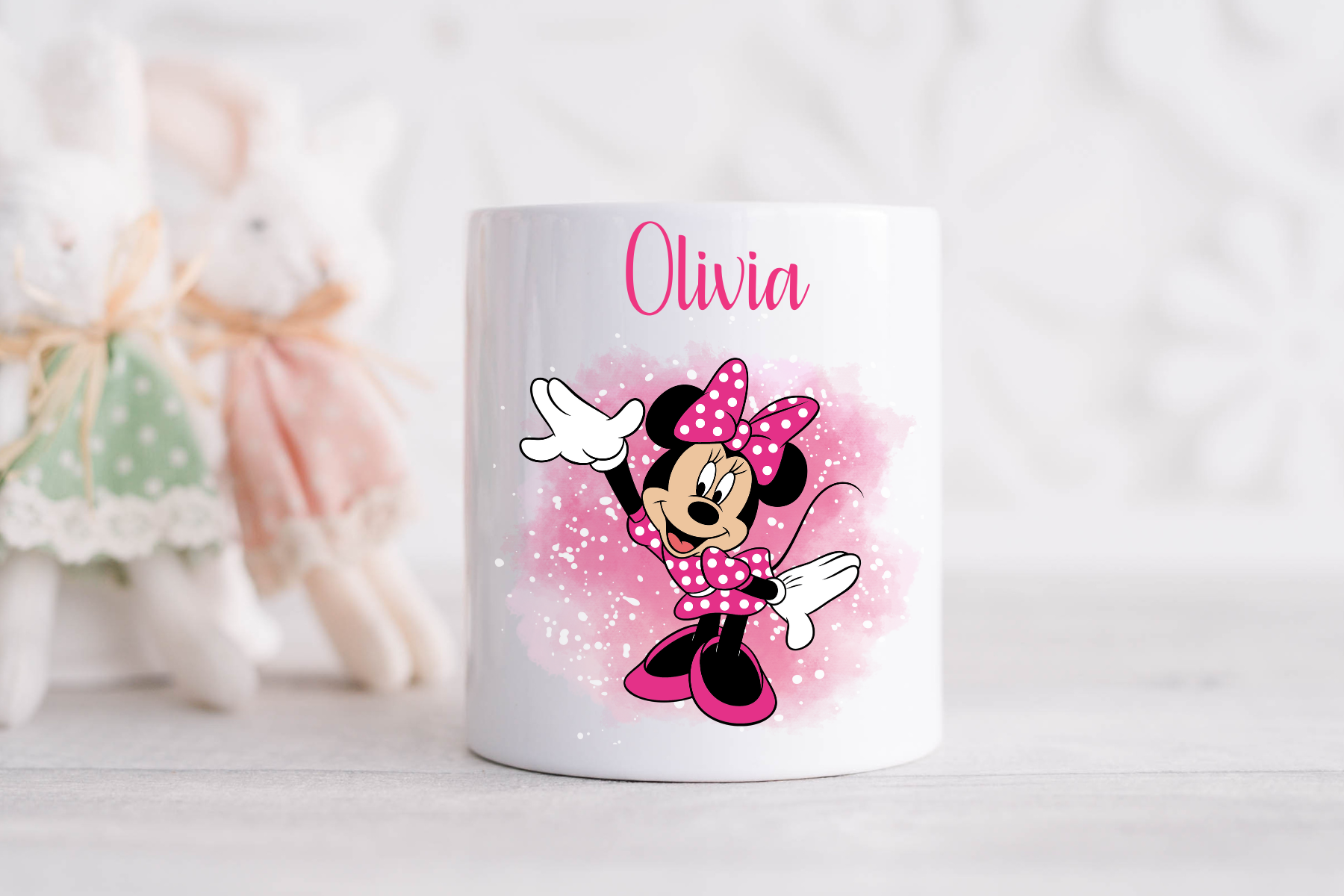A glossy white ceramic money box with a personalised name 'Olivia' and the Minnie Mouse character design, featuring pink and black colors with glitter accents.
